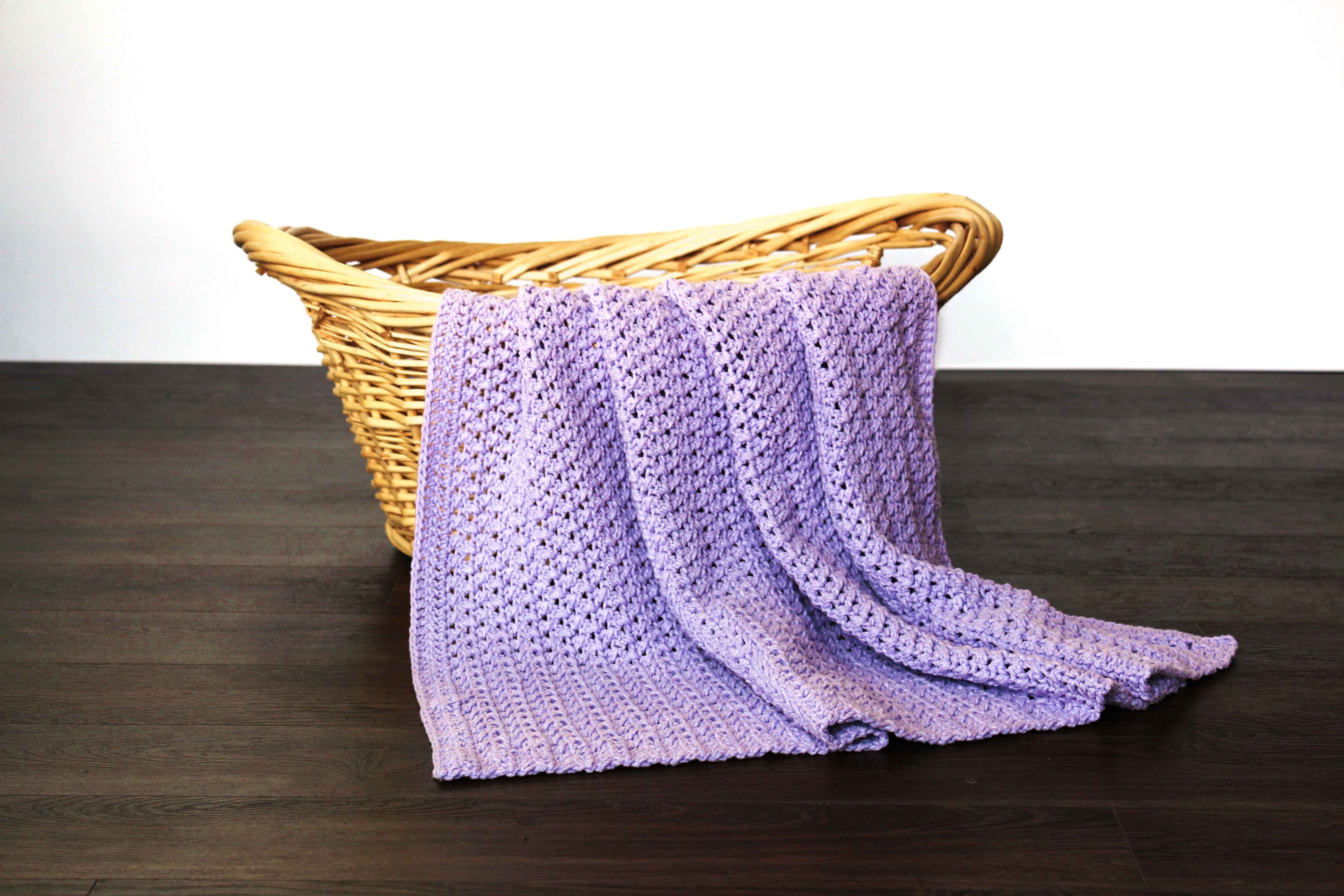 Purple baby blanket featuring a textured criss cross pattern being displayed on a wicker basket