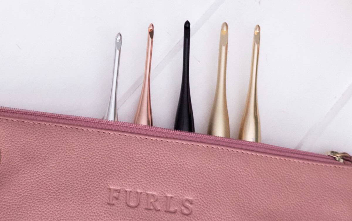 Furls Streamline Metal crochet hooks displayed alongside the Blair Leather Hook Clutch, arranged in a flat lay.