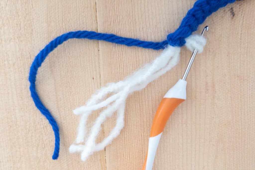 Close-up of a crochet hook attaching white yarn strands to the foundation single crochet (FSC) section of a crochet gnome to form the beard.