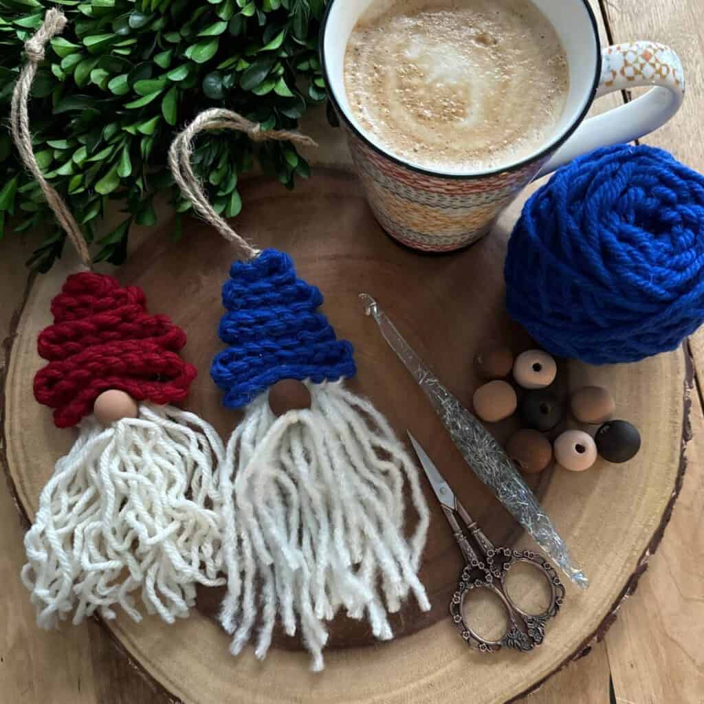 Flat lay of a cozy crochet setup with a latte, greenery, a ball of blue yarn, two finished gnomes, a sparkly crochet hook, and an assortment of wooden beads in porcelain, almond, caramel, and mocha skin tones.