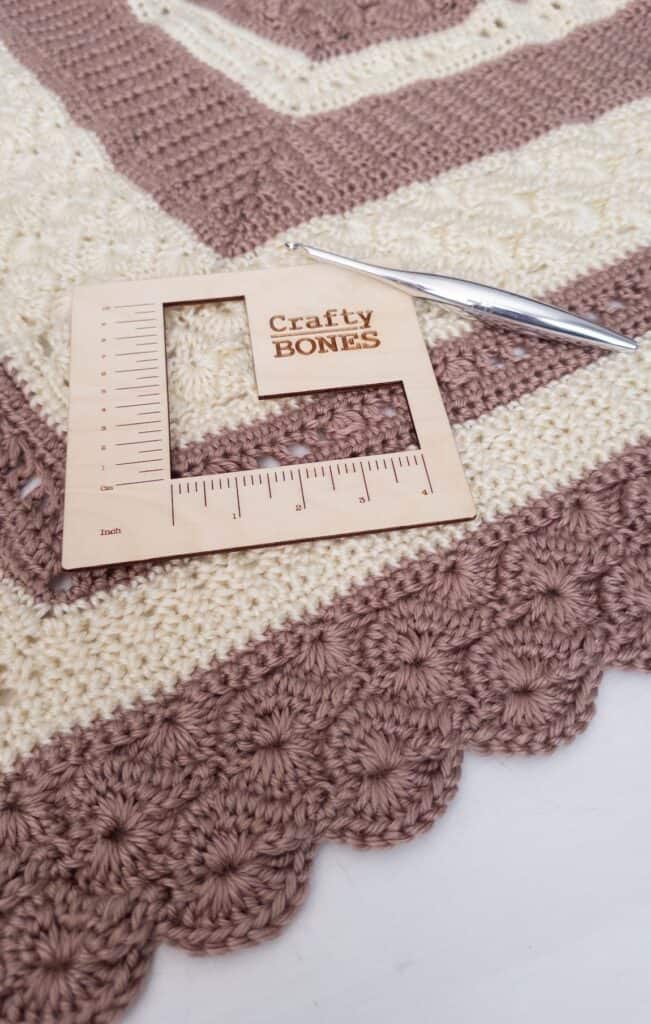 Shell and Lace crochet throw blanket with a wood square gauge ruler with crafty bones logo with a metal streamline crochet hook