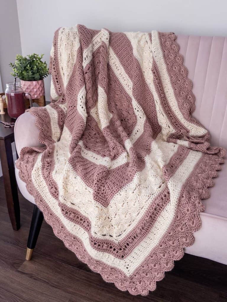 Heirloom crochet blanket with scalloped edges in rose and cream yarn, draped over a blush-colored couch.