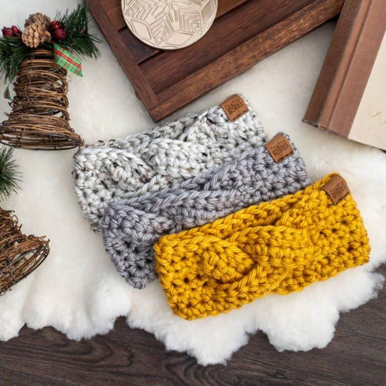 Three braided crochet earwarmers in yellow, gray, and off-white, displayed with holiday décor and a cozy setup.