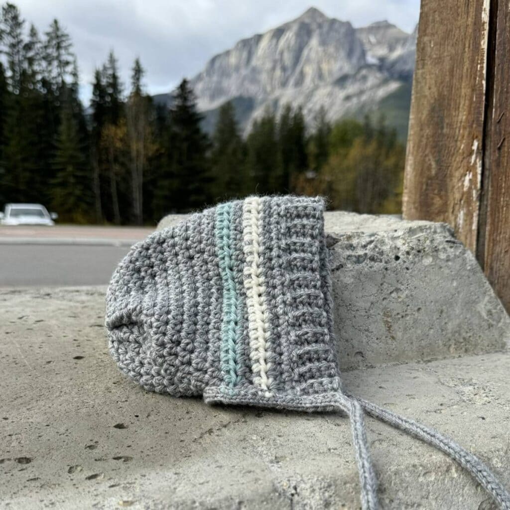 Grey kids bonnet laying on concrete with mountains in the background