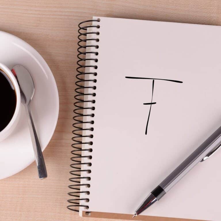 Flat lay photo of a handwritten double crochet chart symbol on paper in a coiled notebook, beside a cup and saucer filled with coffee.