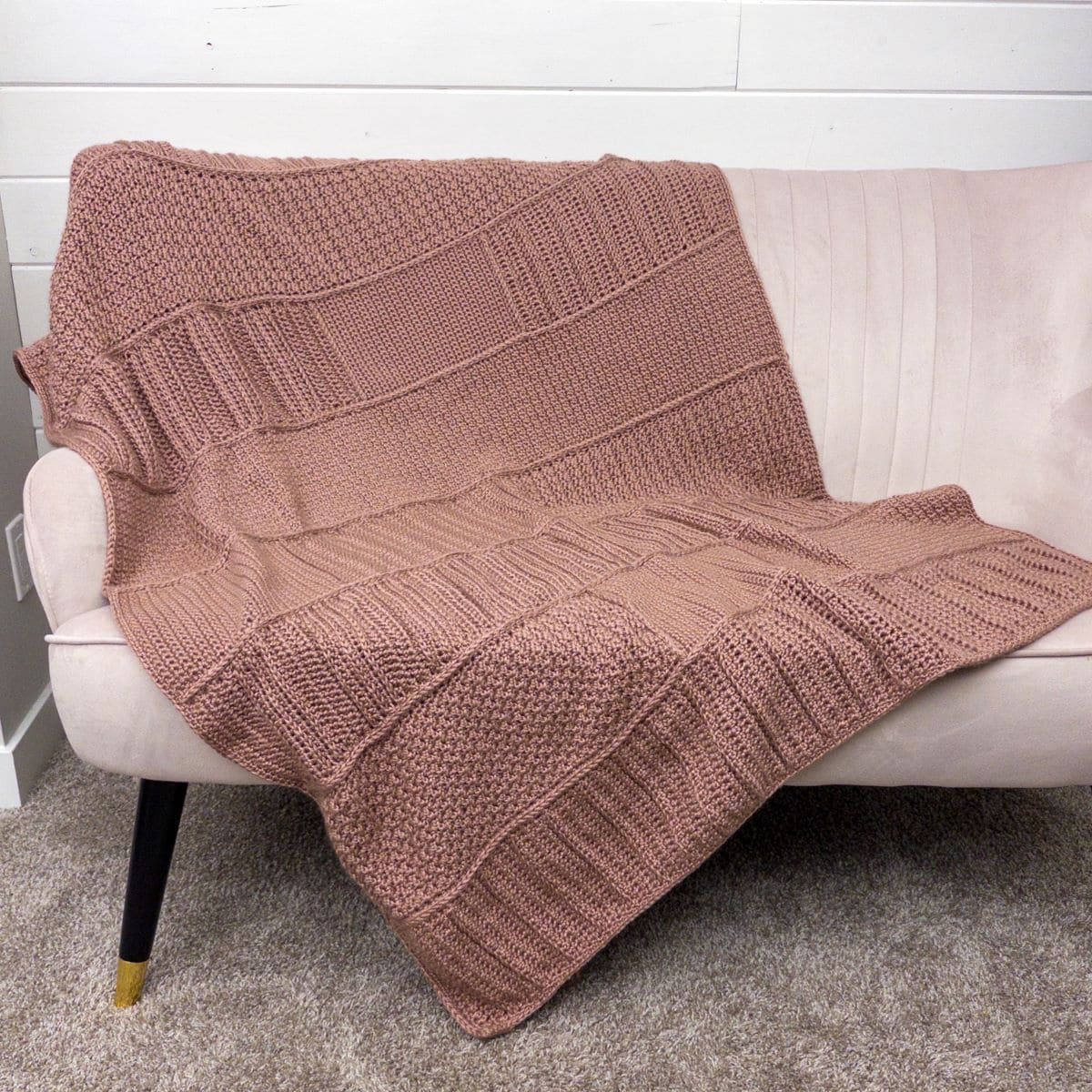 Handmade crochet blanket draped over a beige sofa in a cozy living room setting.