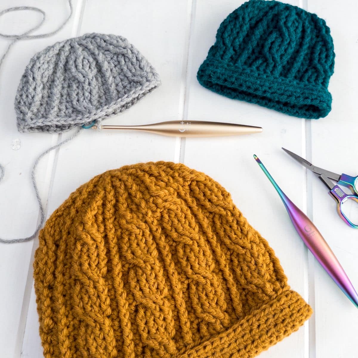 Layflat of the Sintra Cabled Crochet Hat showing textured cable stitches and double brim construction alongside crochet tools.